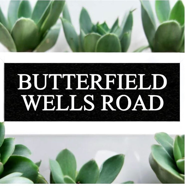 A black square House Sign with clear deep-cut numbers featuring a green plant placed elegantly on its surface www.HouseSign.co.uk