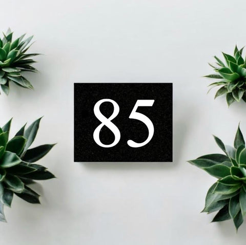 A black square House Sign with clear deep cut numbers featuring a green plant placed elegantly on its surface www.HouseSign.co.uk