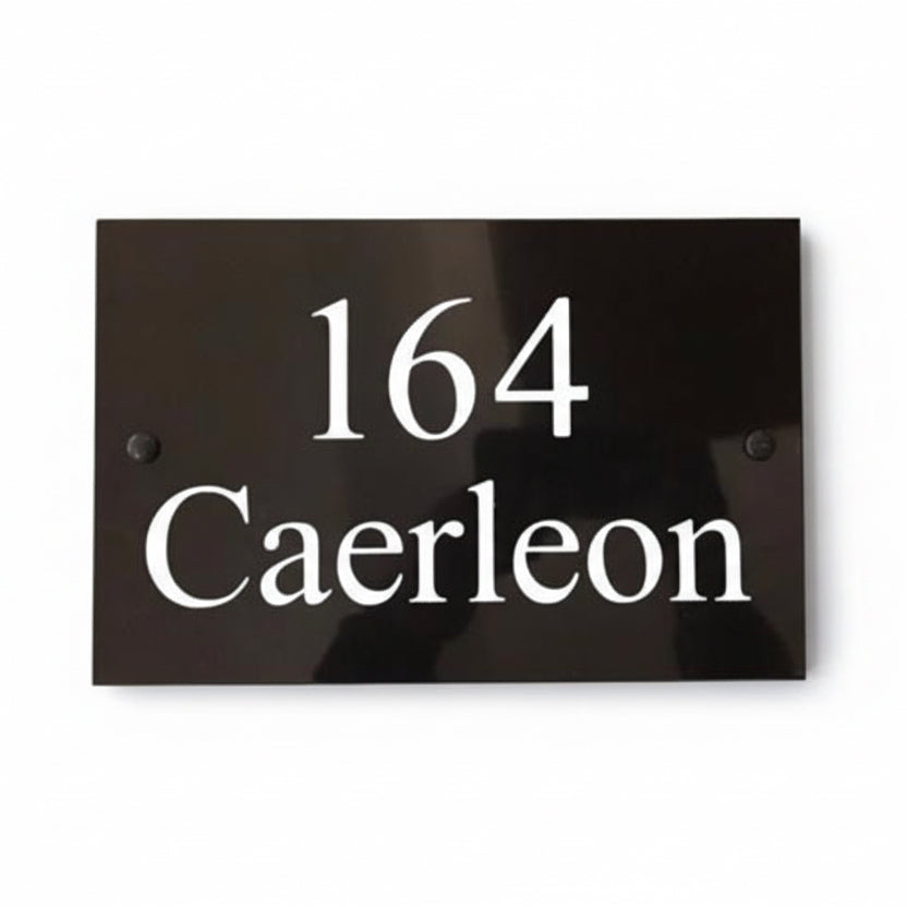 A black square House Sign with clear deep cut numbers featuring a green plant placed elegantly on its surface www.HouseSign.co.uk