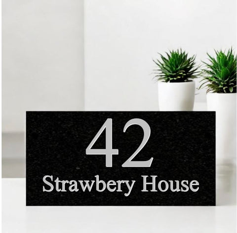 A black square House Sign with clear deep-cut numbers featuring a green plant placed elegantly on its surface www.HouseSign.co.uk 