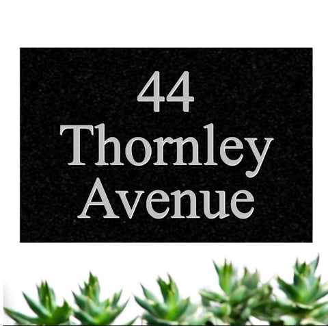 A black square House Sign with clear deep cut numbers featuring a green plant placed elegantly on its surface www.HouseSign.co.uk 