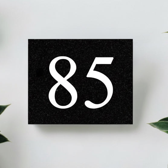 A black square House Sign with clear deep cut numbers featuring a green plant placed elegantly on its surface www.HouseSign.co.uk 