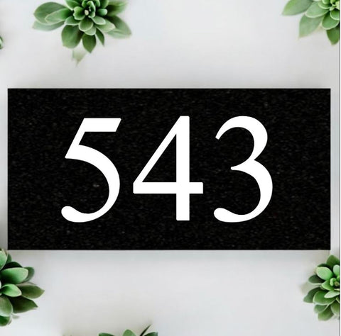 A black square House Sign with clear deep-cut numbers featuring a green plant placed elegantly on its surface www.HouseSign.co.uk 