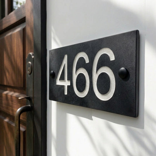 Natural slate house number 466 sign with white carved lettering on a white wall beside a wooden door.