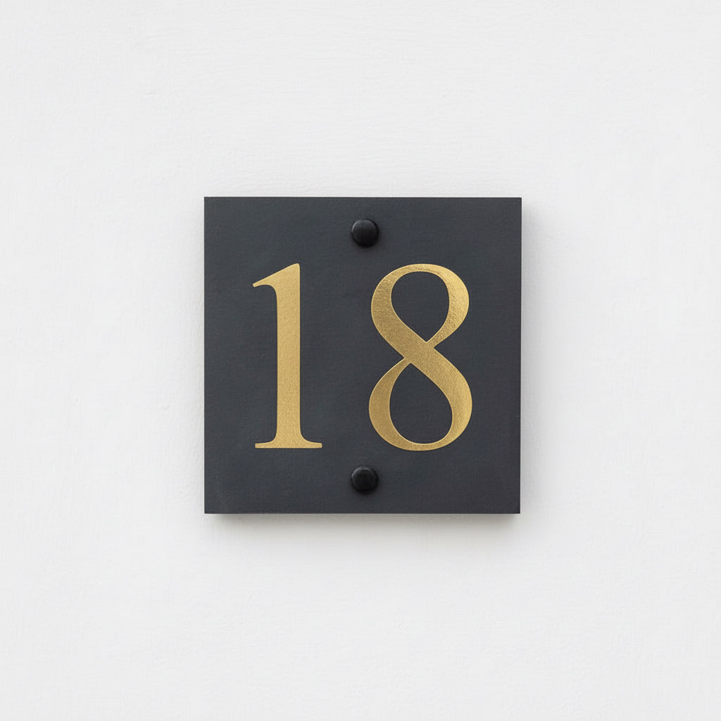 The picture shows a slate house sign with numer 18 in white on a white painted background